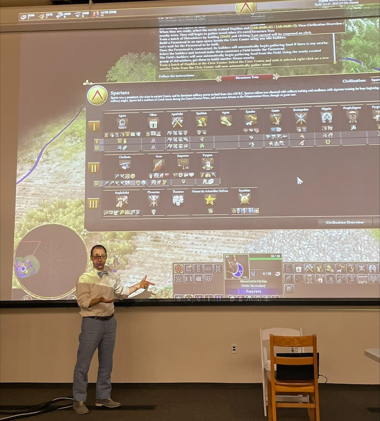 The author Corey Stephan introduces 0̸ A.D. to his university-level ancient Greek class via a projector screen, specifically showing the technological tree of the Spartan civilization.